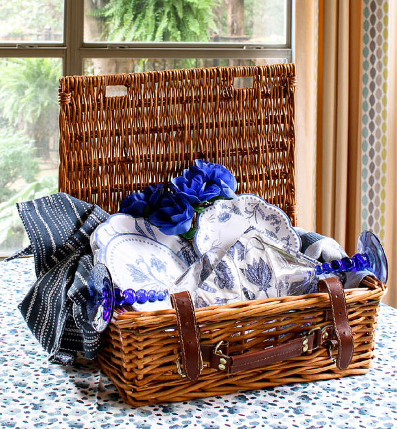 idea for decorating basket brown picnic basket with blue and white plates and napkins and blue flowers on blue tablecloth