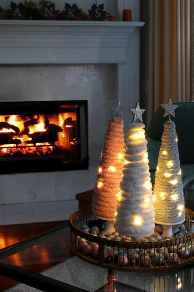DIY yarn Christmas trees in front of fireplace with lights