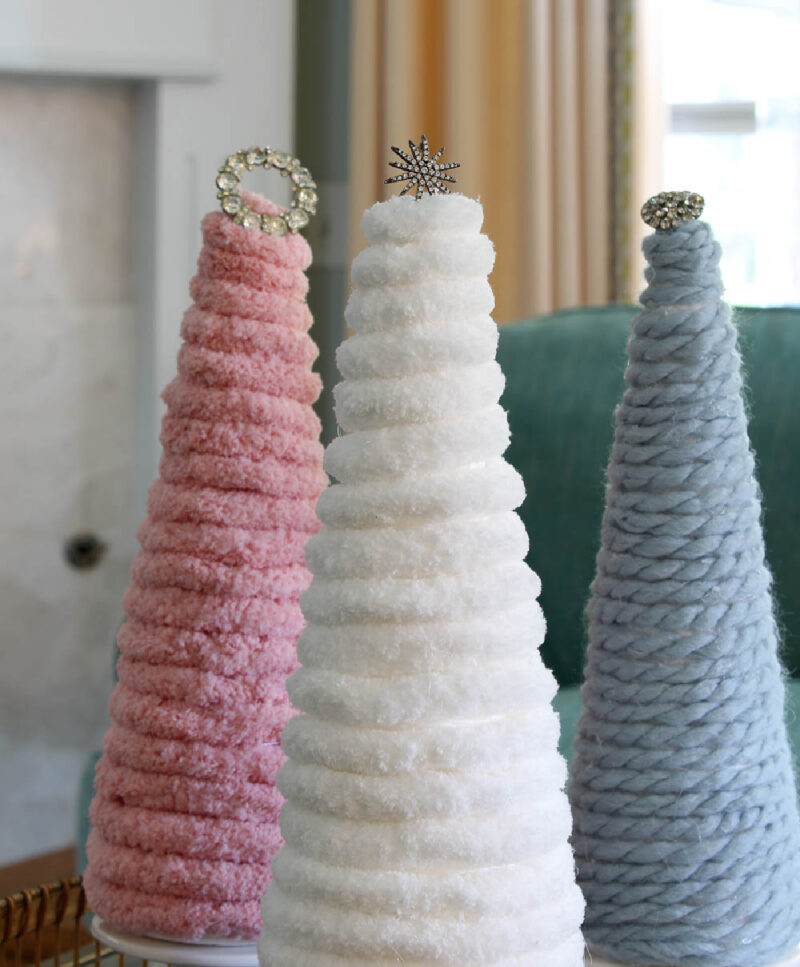 three yarn Christmas trees in pink, white, and blue