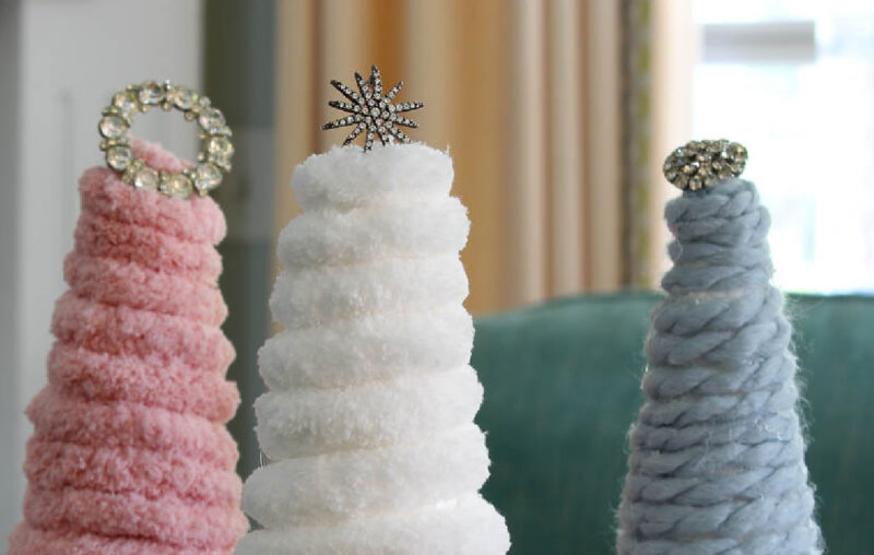 three yarn Christmas trees in pink, white, and blue with rhinestone toppers