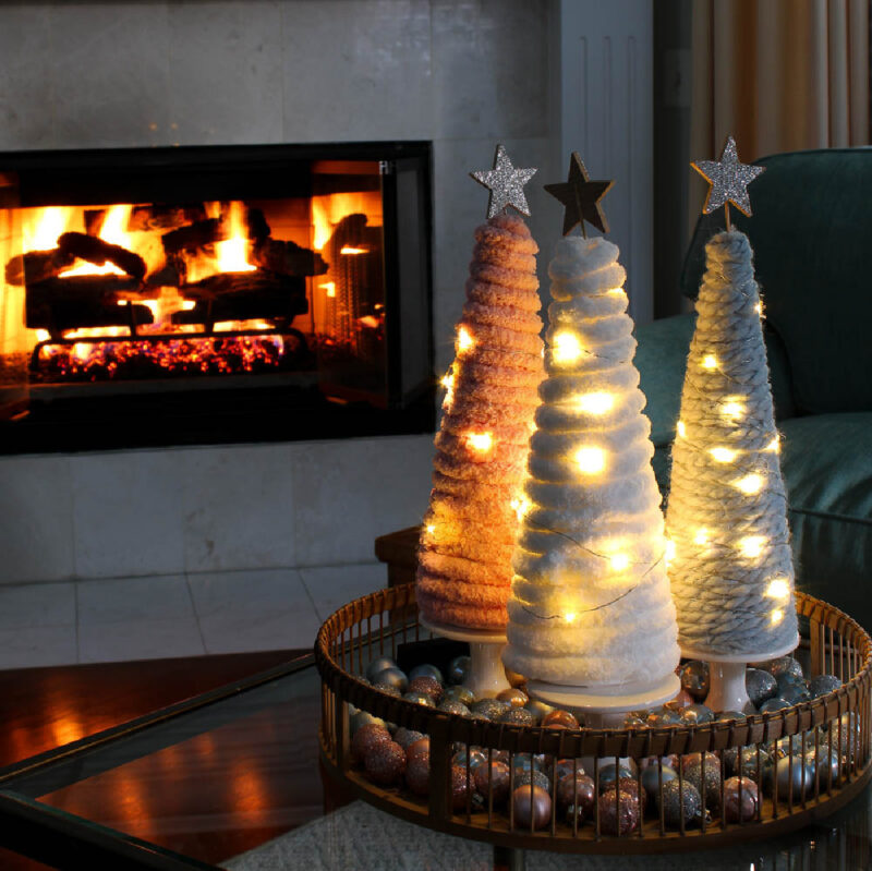 DIY yarn Christmas trees in front of fireplace with lights