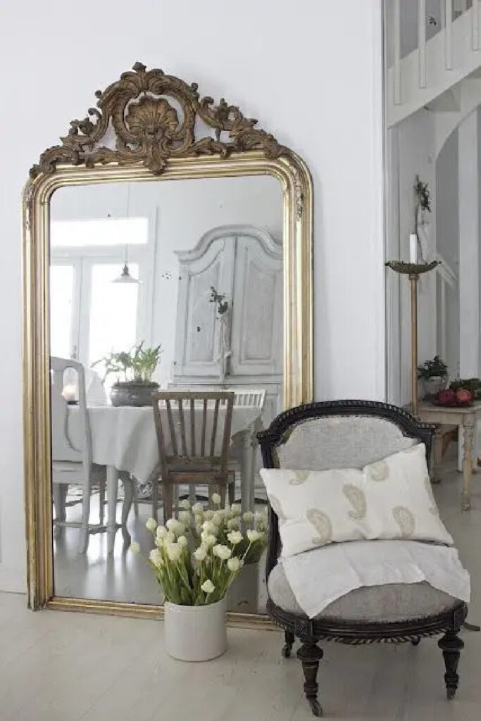 oversized mirror with gold trim and planter of white tulips and chair