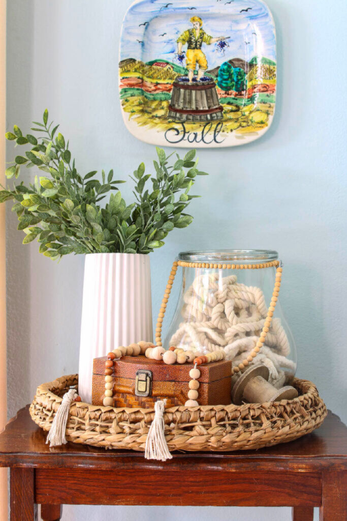 large glass vase vignette with greenery in white vase on a round woven basket