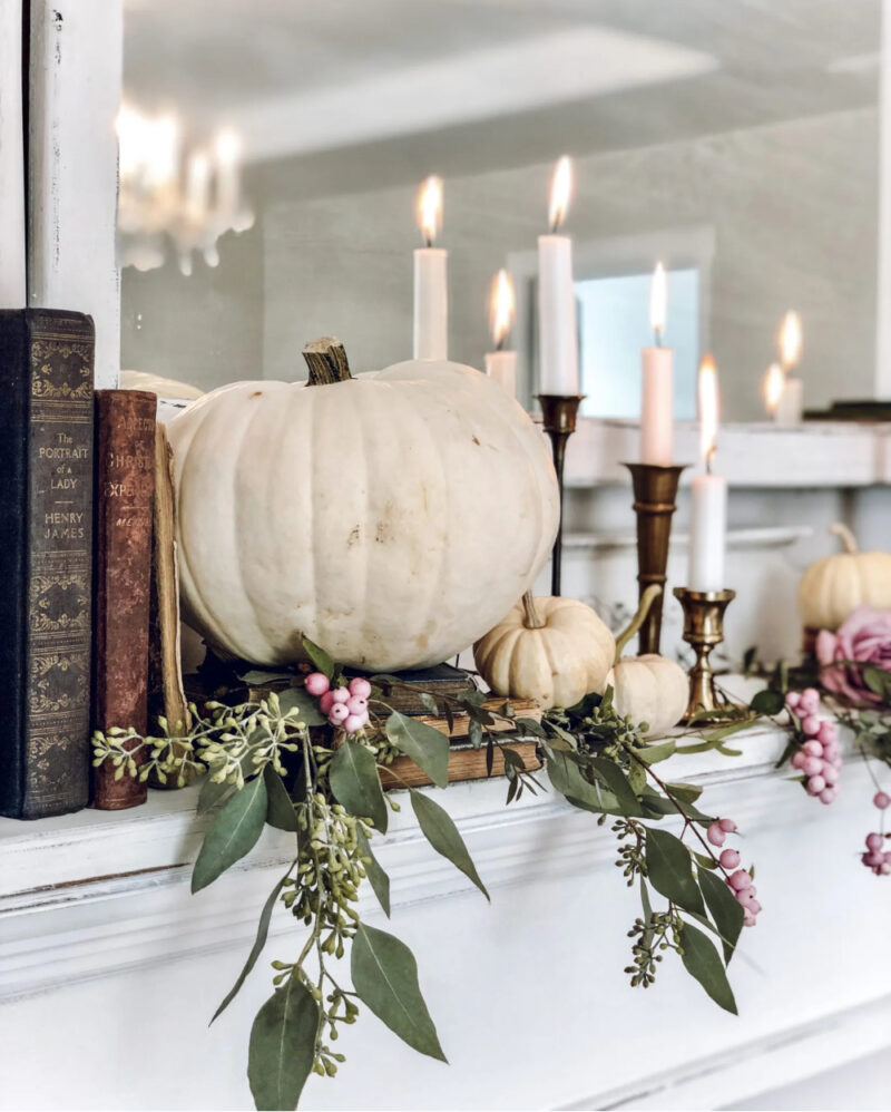 fall mantel with pumpkins, green foliage, and books