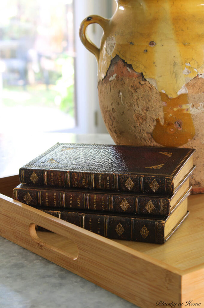 yellow chrysanthemums in confit pot on wood tray with stack of 3 dark brown books