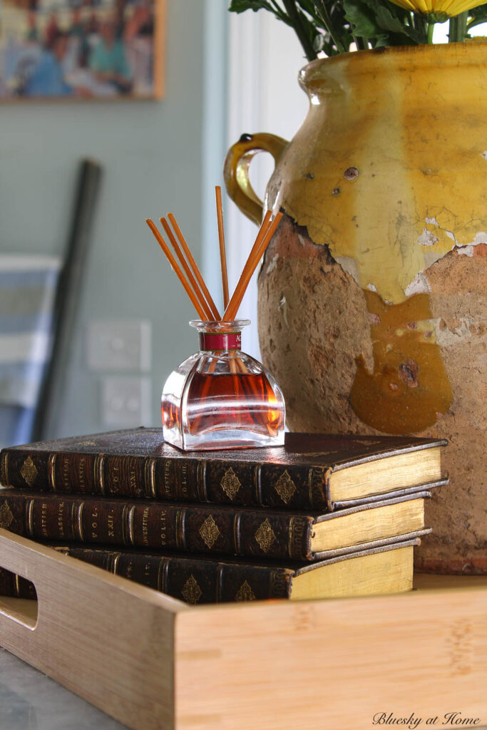 confit pot on wood tray with stack of 3 dark brown books with small bottle of infused oil