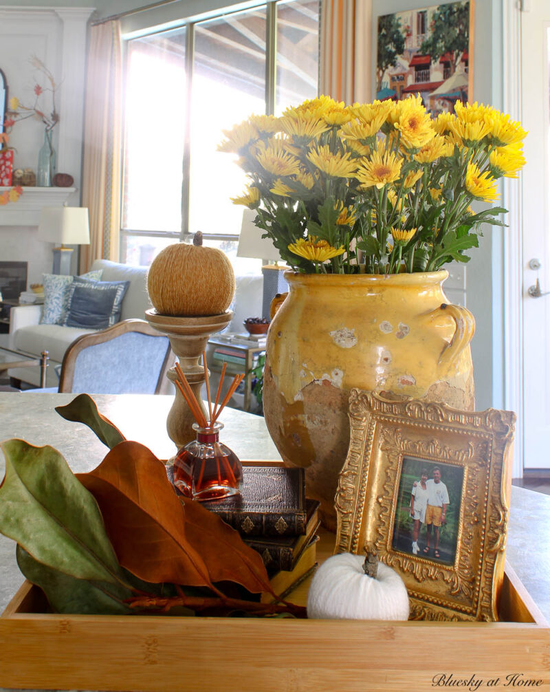 fall vignette with confit pot, orange pumpkin, stack of brown books, and gold frame.