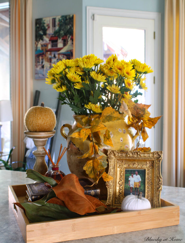 fall vignette with confit pot, orange pumpkin, stack of brown books, and gold frame.