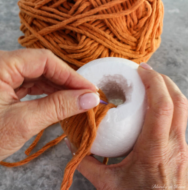 wrapping orange yarn around white styrofoam ball