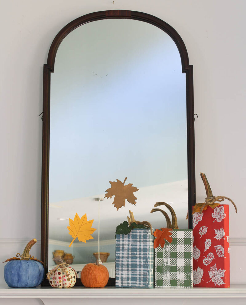 red, blue, and green wood block pumpkins on mantel with glass jar and leaf branches