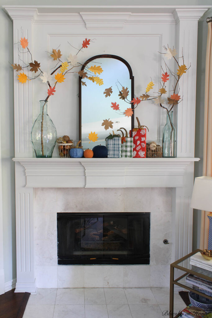 red, blue, and green wood block pumpkins on mantel with glass jar and leaf branches
