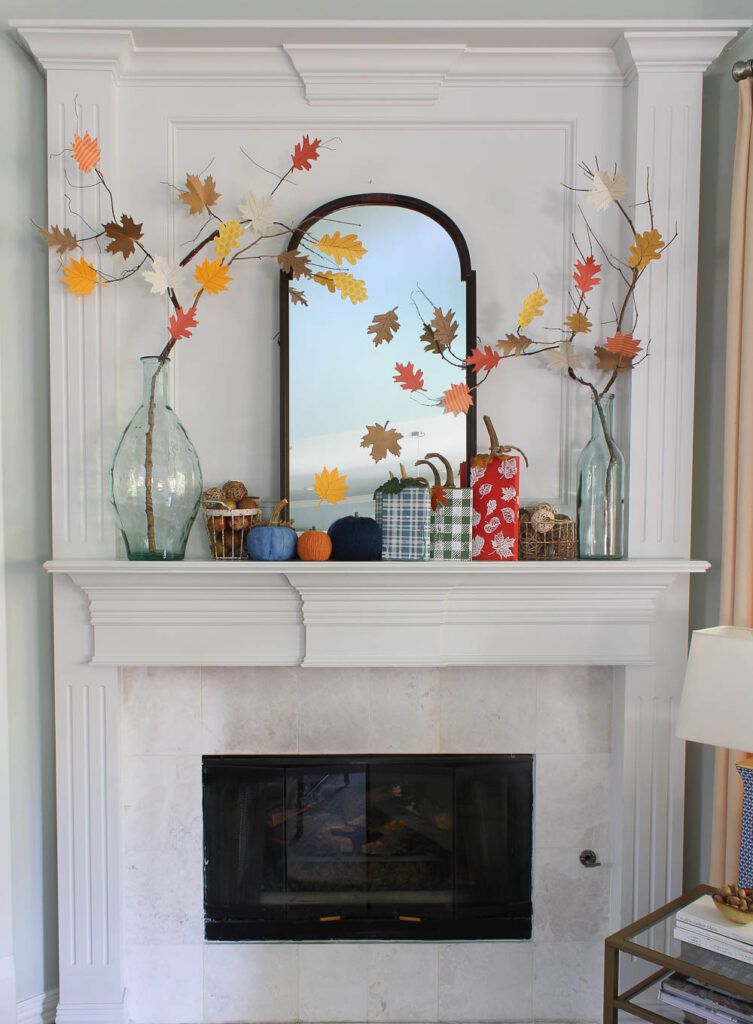 red, blue, and green wood block pumpkins on mantel with glass jar and leaf branches