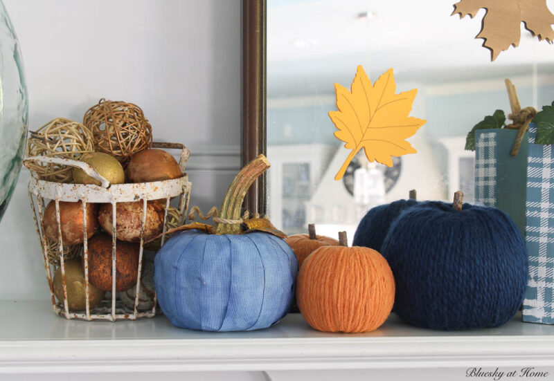 yarn pumpkins in blues and orange on mantel with glass jar and leaf branches