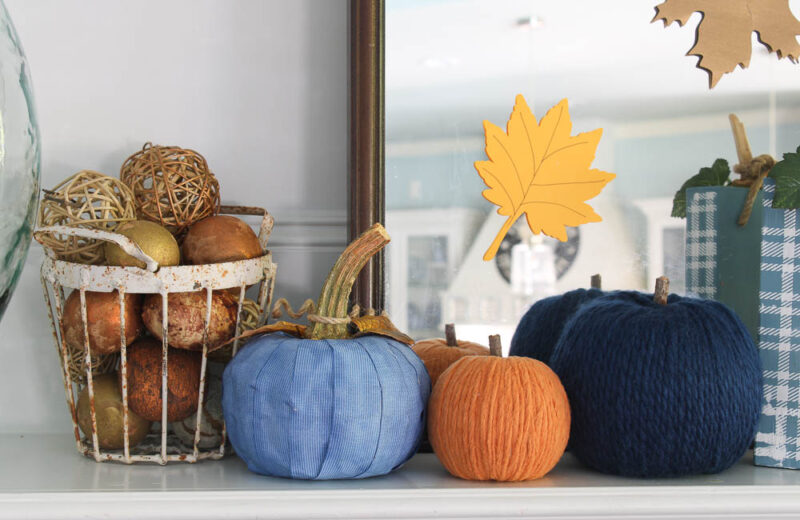 yarn pumpkins in blues and orange on mantel with glass jar and leaf branches