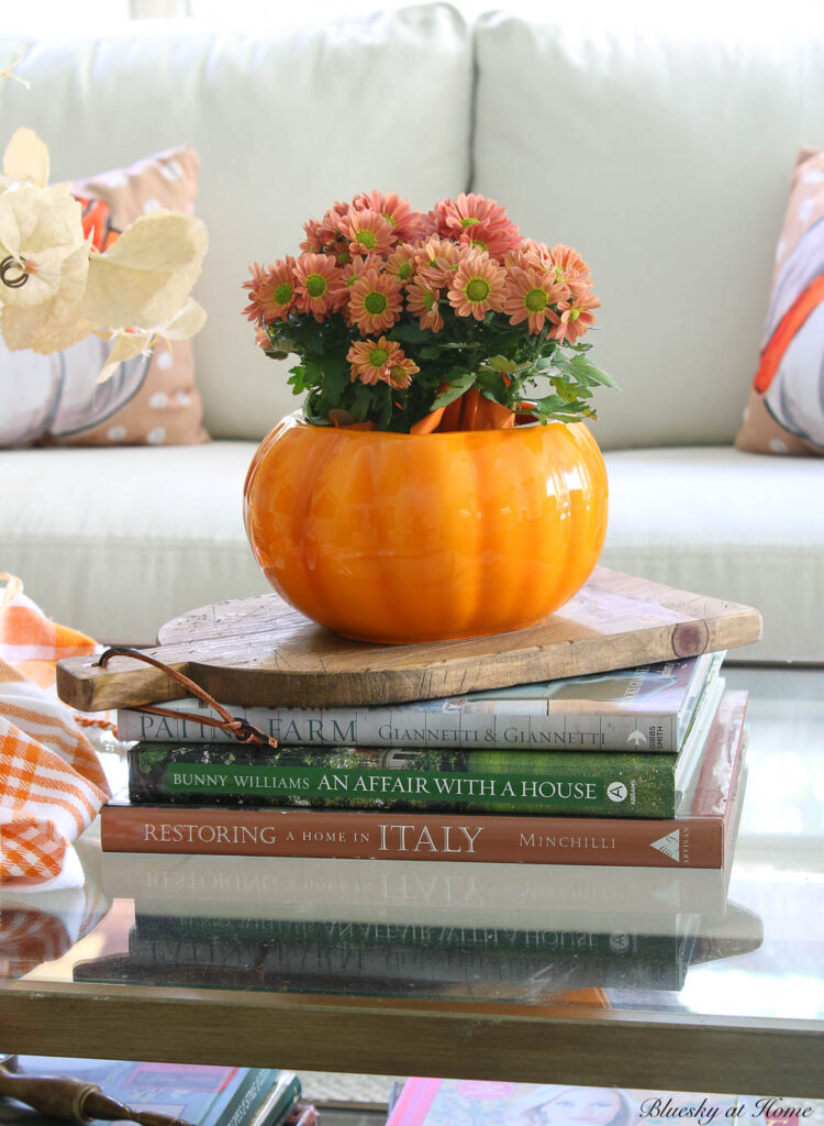 coral chrysanthemums in ceramic orange pumpkin on wood cutting board on stack of books