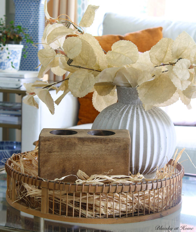 round basket with raffia in front of white sofa with white vase and cream faux leaves and sugar mold