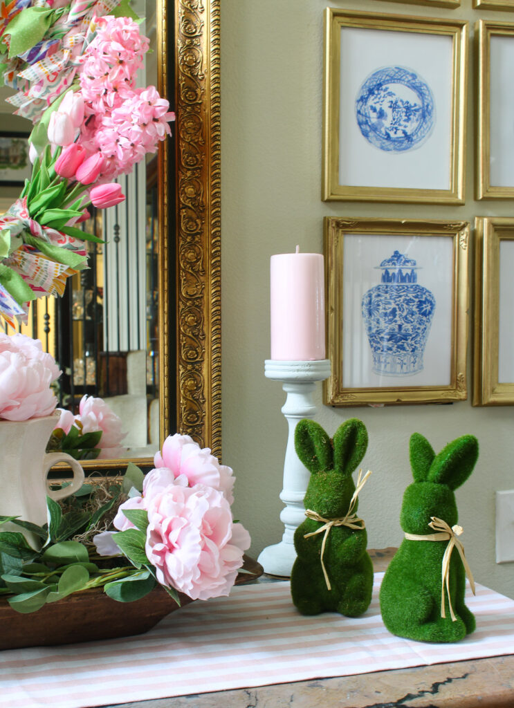 green bunnies with spring wreath hanging on a mirror with pink peonies in white container on console table