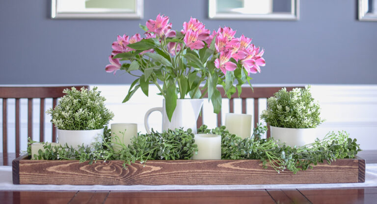 pink spring floral centerpiece on a wood tray with candles and greenery.