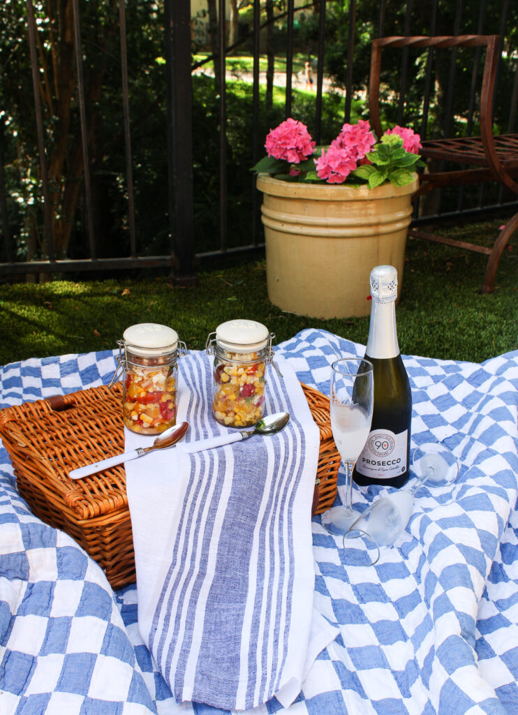 picnic with summer summer salad in a jar and a bottle of Prosecco on blue check quilt