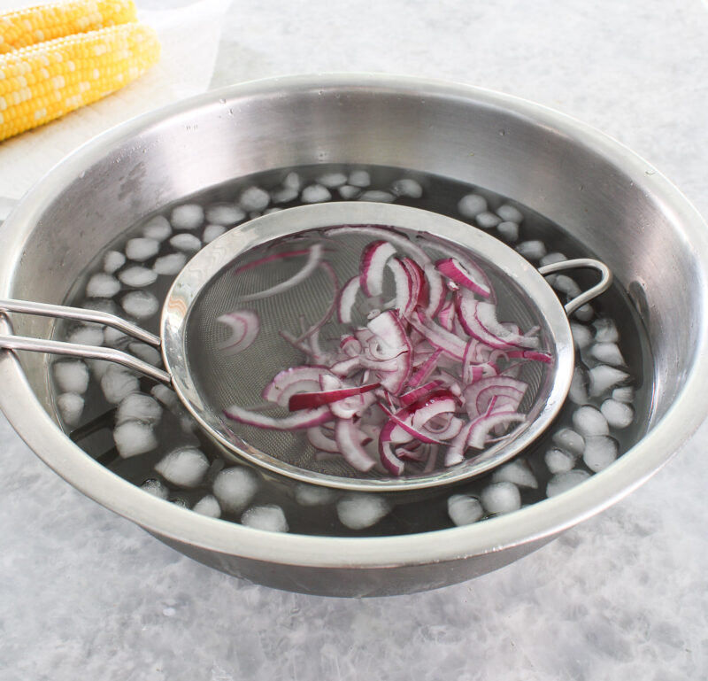 sliced red onion in bowl of ice water