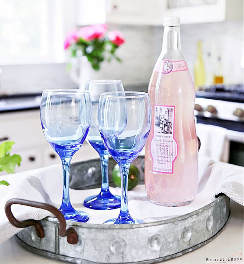 galvanized tray with blue wine glasses and a bottle of pink liquid on a kitchen counter