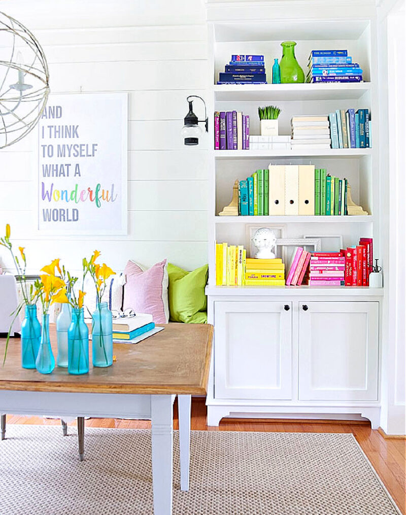 cabinet and bookshelves filled with colorful books in blues, greens, yellows, and pinks and aqua bottles on a wood table