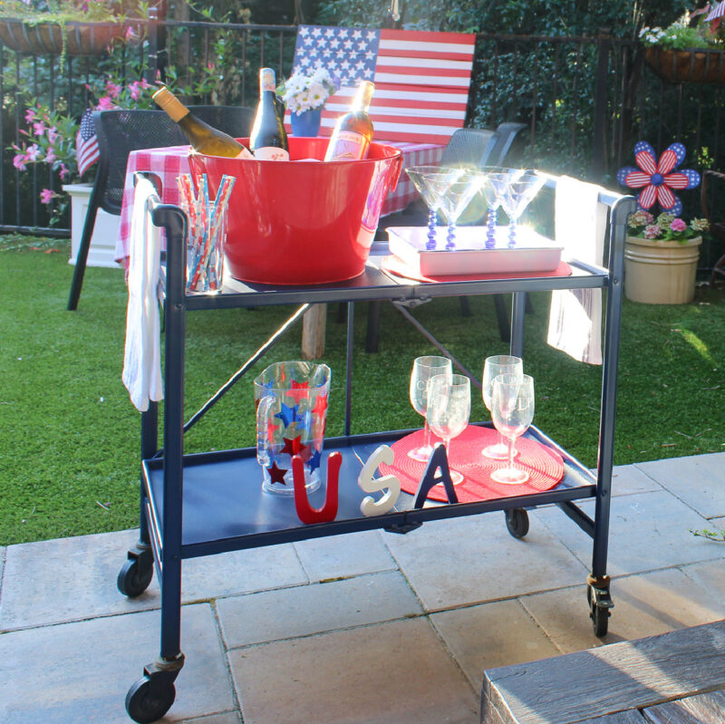 bar cart on patio with red ice bucket and red, white, and blue tableware