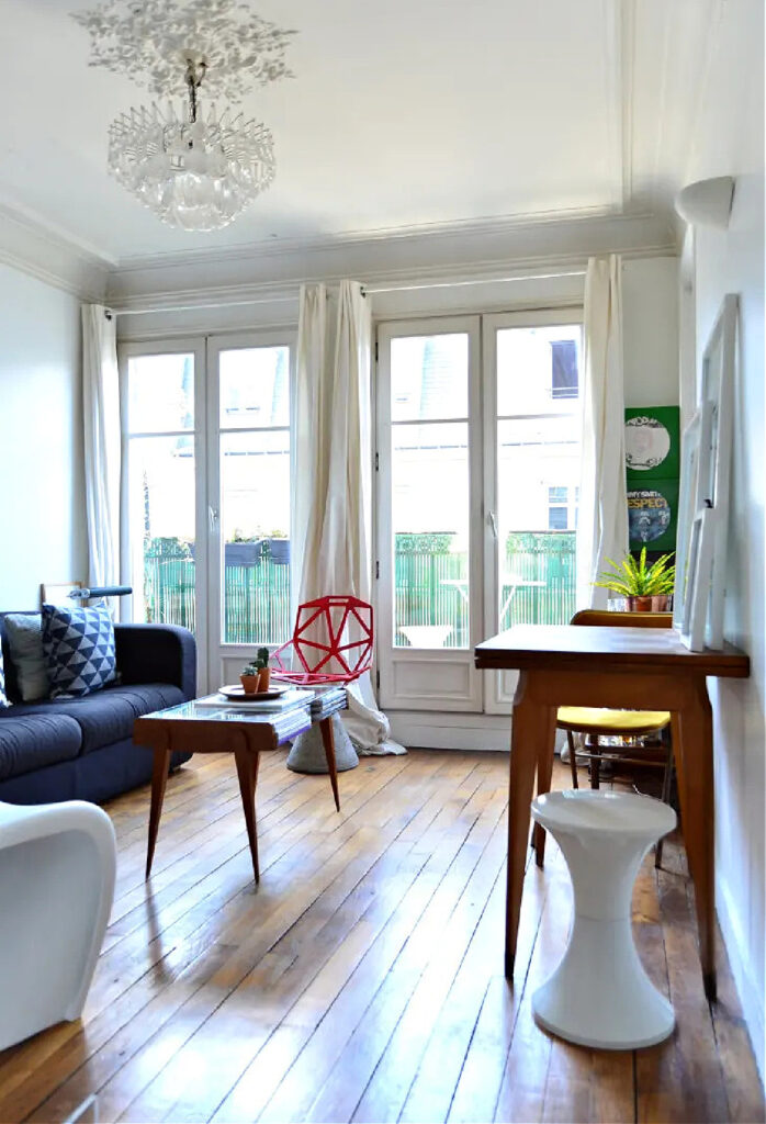 living room with brown hardwood flowers and large window with white drapes and a navy blue sofa