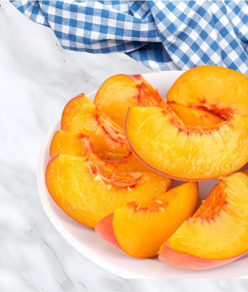 sliced peaches in white bowl with blue dish towel