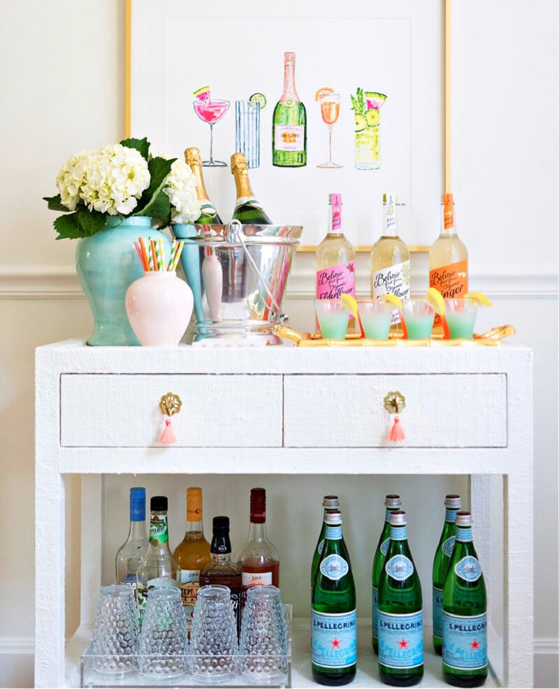 white side table with bottles and ice bucket and a pale blue vase of white hydrandeas set up as a bar cart