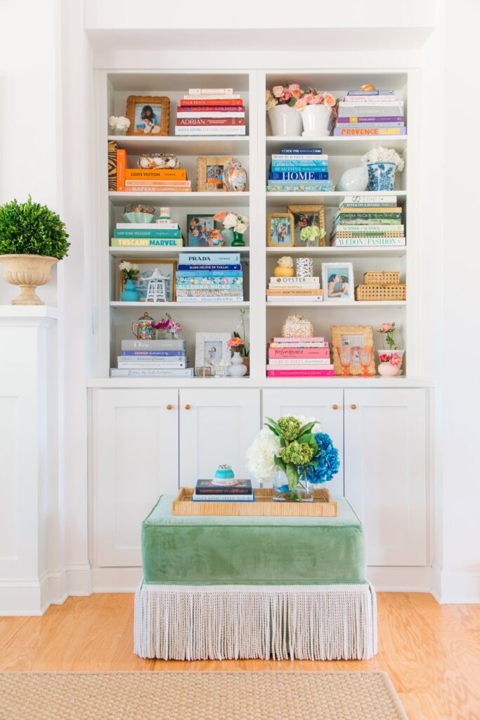 cabinet and bookshelves filled with colorful books in blues, greens, orange, and pinks and green ottoman in front