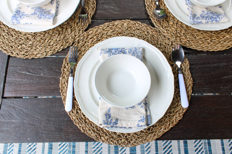 white dishes on woven placemats with blue toile napkins