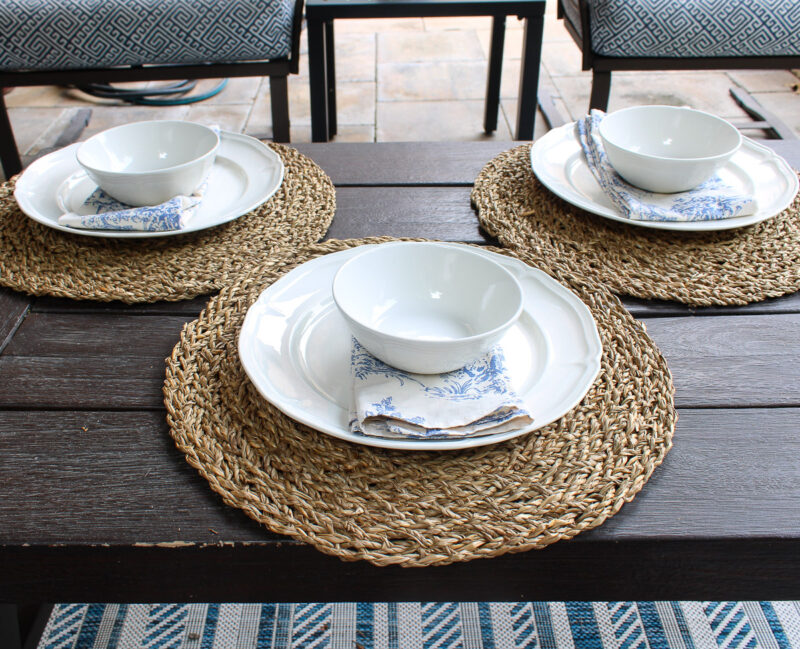 white dishes on woven placemats with blue toile napkins