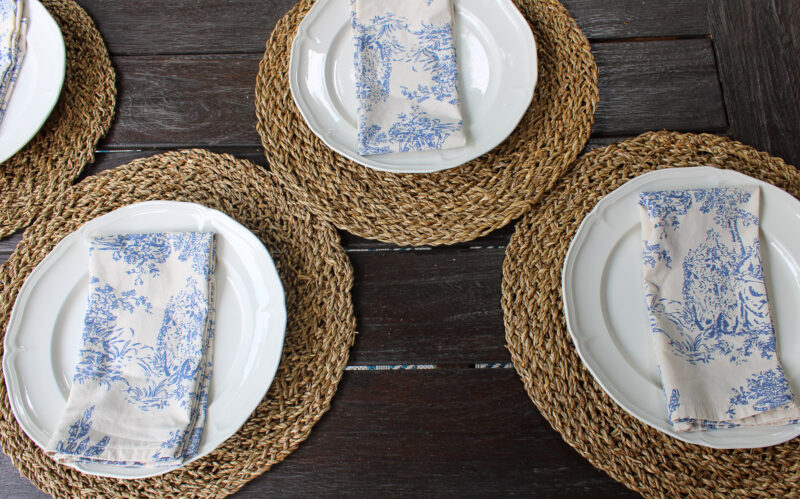 white dishes on woven placemats with blue toile napkins