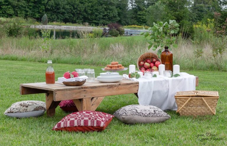 wood table outside on grass with pillows and apples for fall table