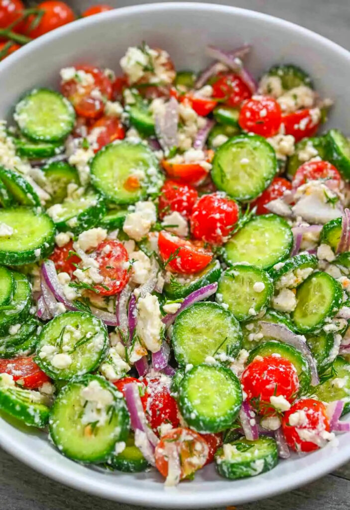 sliced cucumber with halved red cherry tomatoes and onion in a white bowl