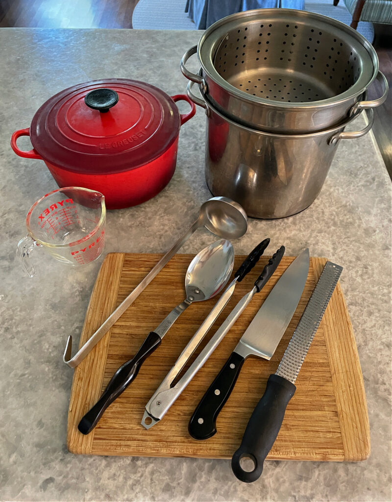 kitchen tools on the kitchen counter to make zucchini pasta recipe: knife, microplante, spoon, tongs, ladle, red Dutch oven, pasta pot, liquid mesuring cup