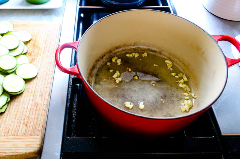 sauteing chopped garlic in a red Dutch oven on the stove top