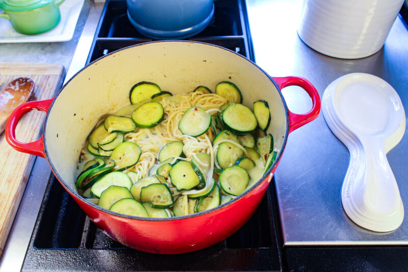 mix of spaghetti and zucchini in a red Dutch oven on a stove top