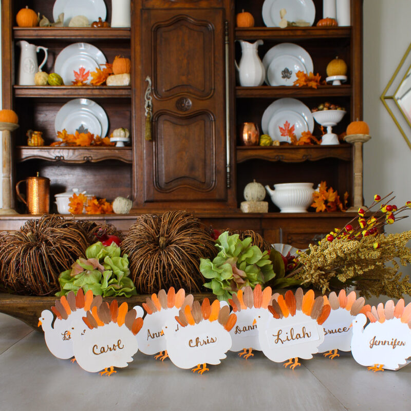 turkey-themed Thanksgiving placecards on dining table with hutch in background