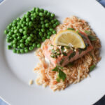 baked salmon with butter sauce on white plate with green peas and orzo