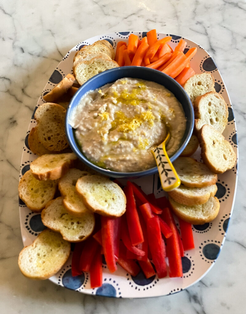 white bean dip in blue bowl on platter with carrots, red bell pepper crudites