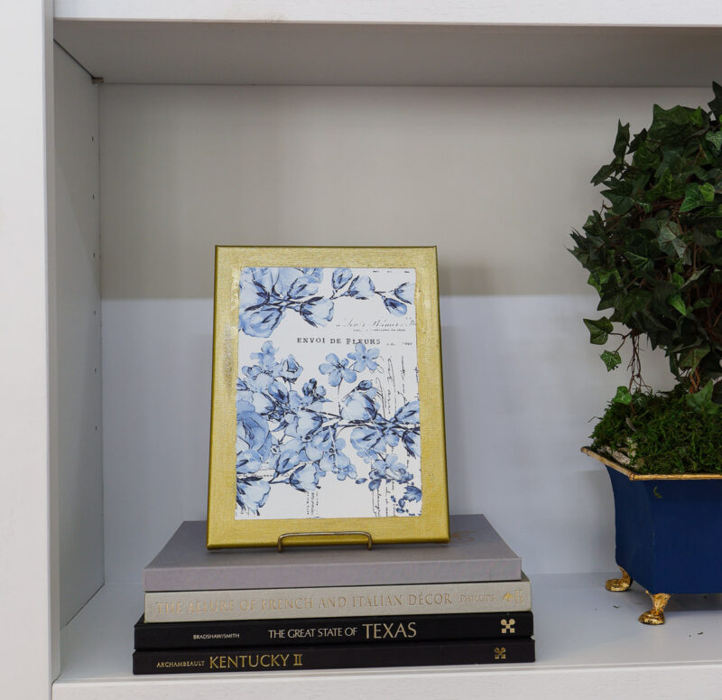 blue transfer art with gold-painted frame on bookshelf