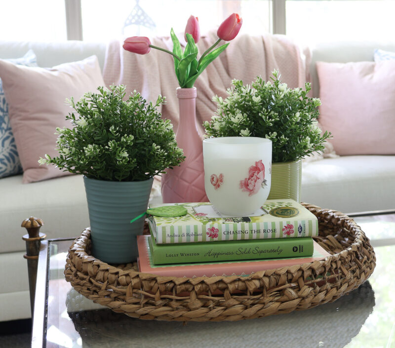 coffee table vignette with woven basket, stacked books, green, blue planters, and pink vase