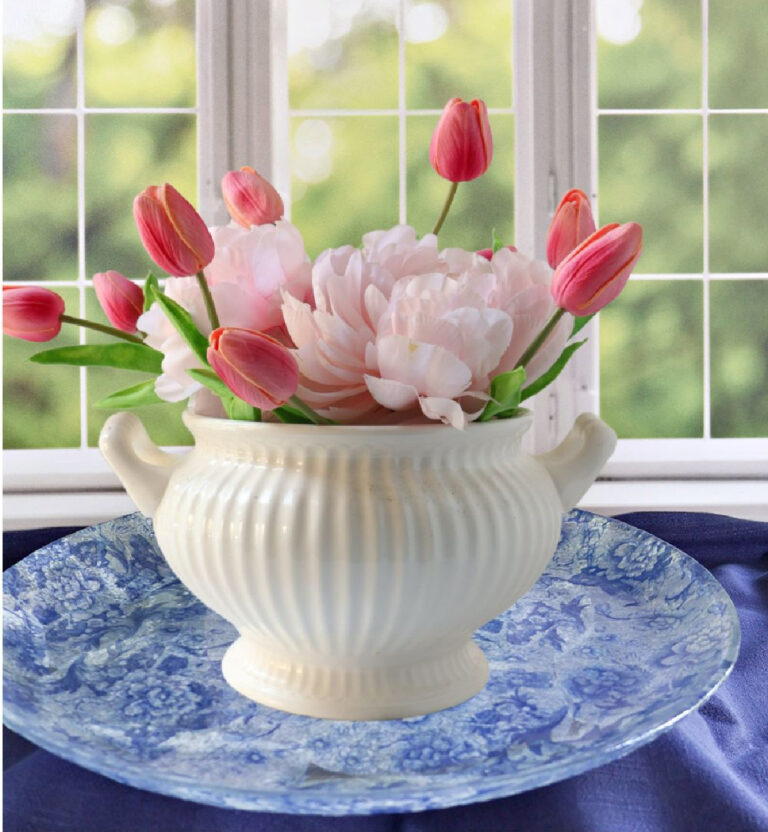 pink flowers in a white tureen on a blue decoupage platter in front of a window