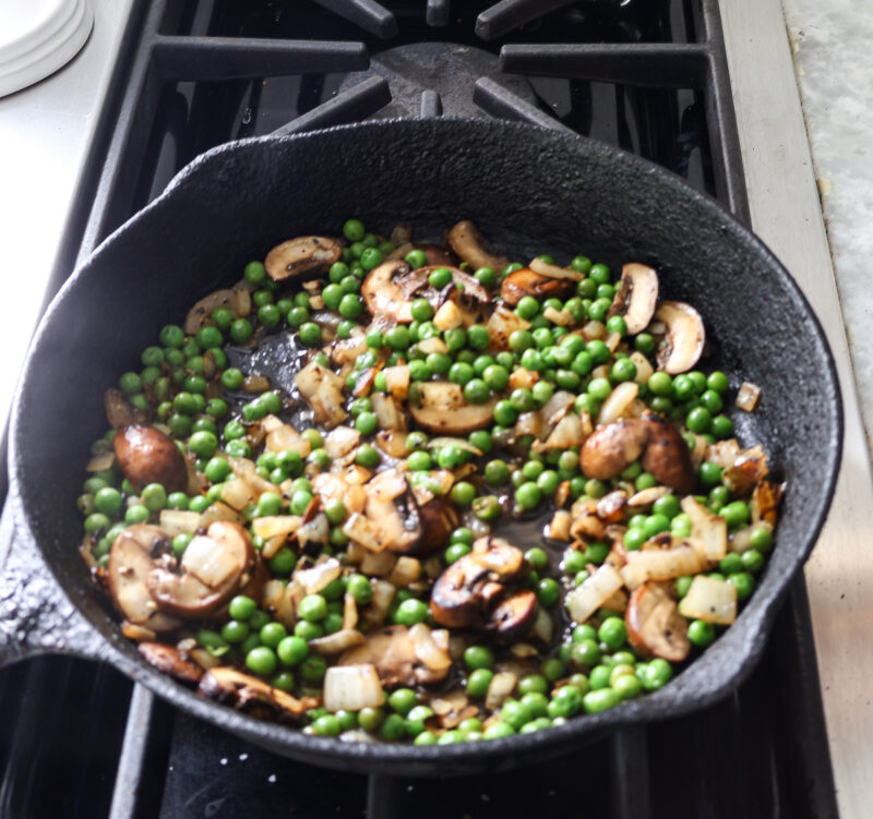 adding peas to mushrooms in cast iron skillet