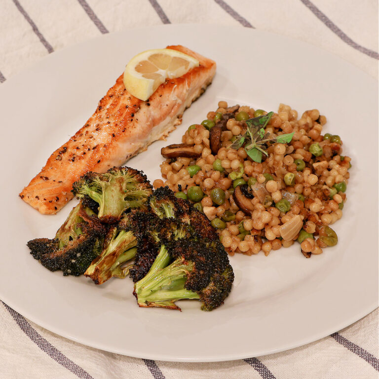 toasted couscous with mushrooms and peas served with salmon and roasted broccoli on white plate