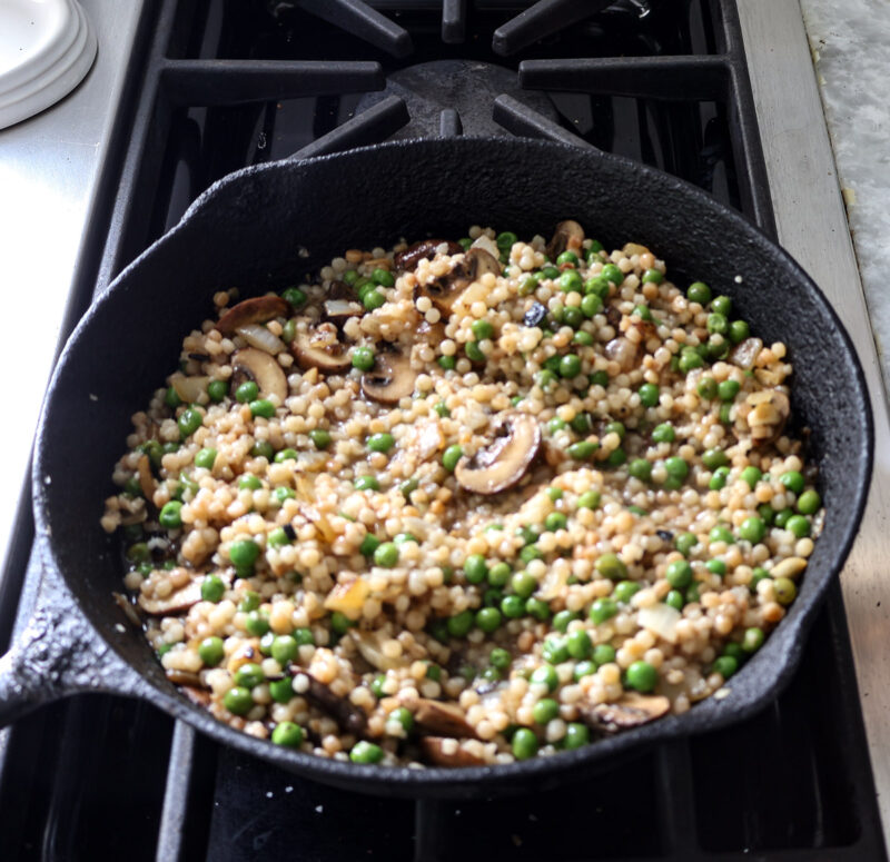 adding toasted couscous to vegetable mixture in skillet