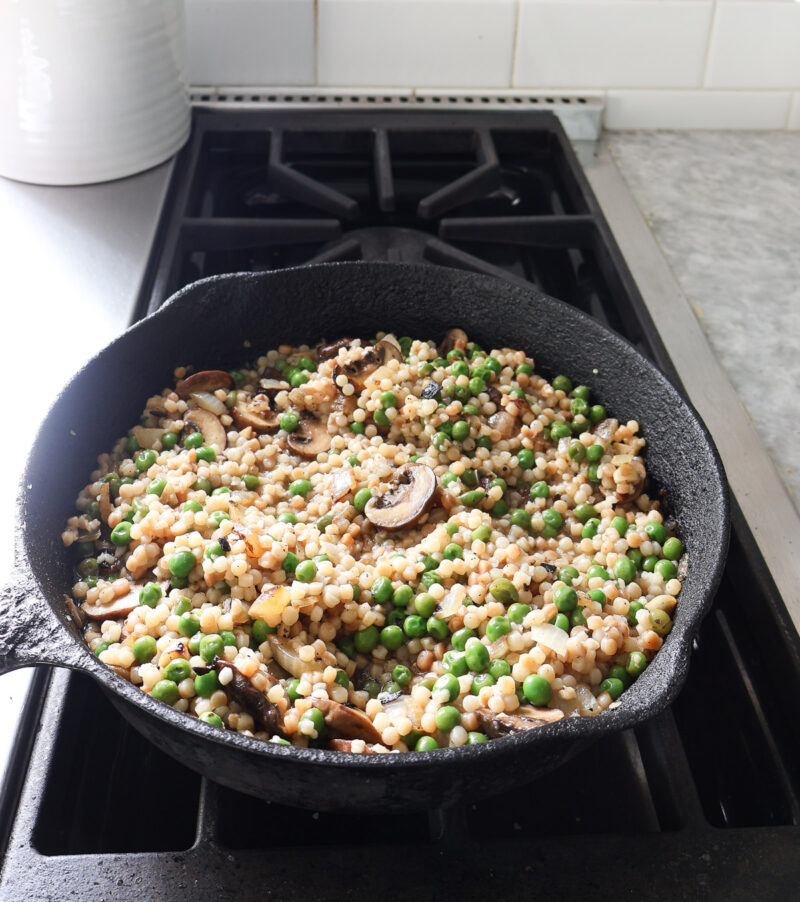 toasted couscous with mushrooms and peas in cast iron skillet