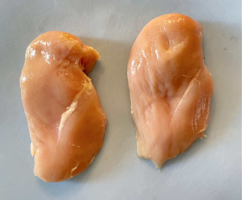 two boneless skinless chicken breasts on blue plastic cutting board